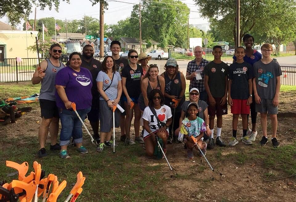 About twenty volunteers of all ages pose outdoors holding litter grabbers, with tools piled in front.