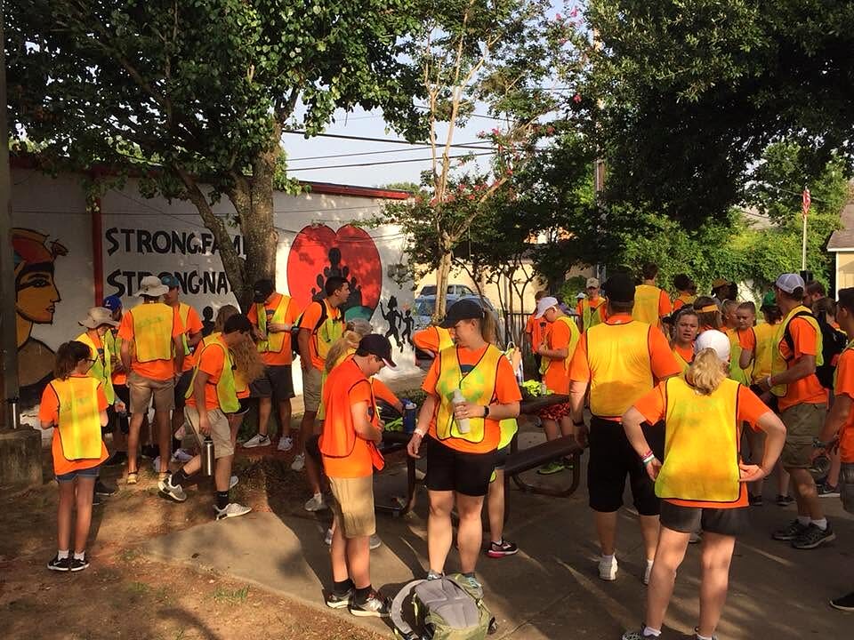 Large group of volunteers in orange and yellow safety vests gathered near a mural before a cleanup.