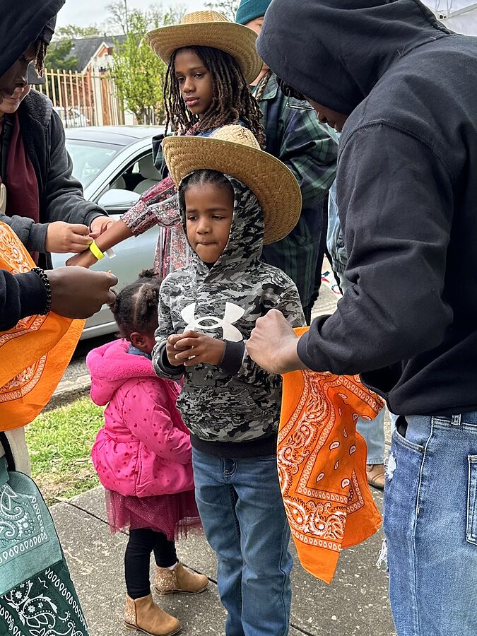 Children in straw hats receiving orange bandanas and wristbands from volunteers at a check-in table.