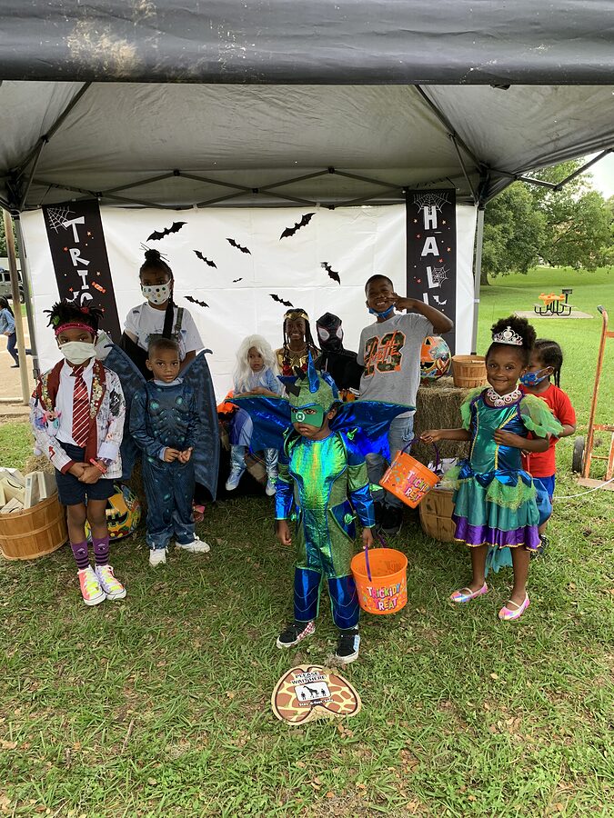 Children in Halloween costumes standing under a canopy tent decorated with bats at a park event.