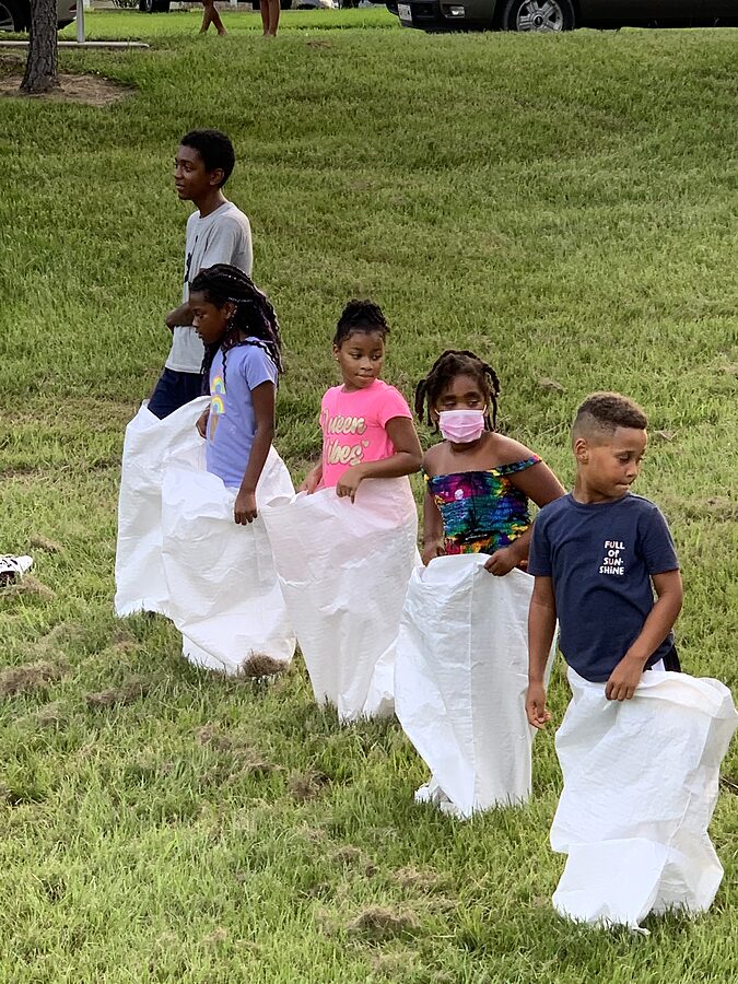 Five children standing in white sacks lined up for a sack race on a grassy field.