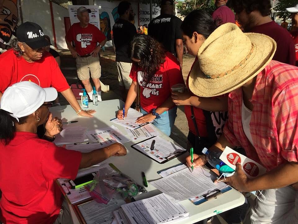 Volunteers in red shirts filling out paperwork at an outdoor sign-in table with clipboards.