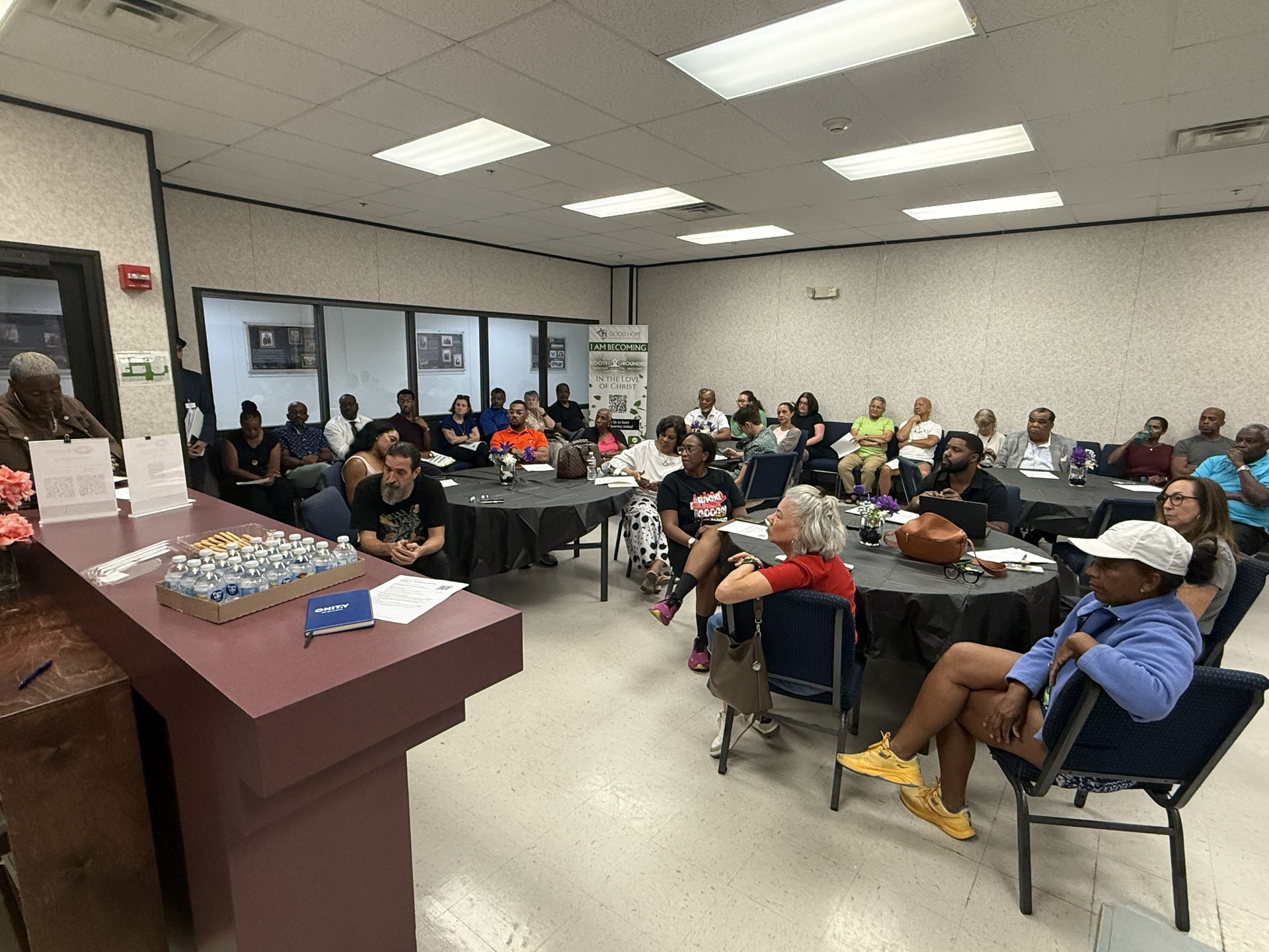 Residents seated around tables and along the wall of the Good Hope Church fellowship hall, some with agendas in hand, facing the podium during the RCA Community Engagement Meeting on October 8, 2026.