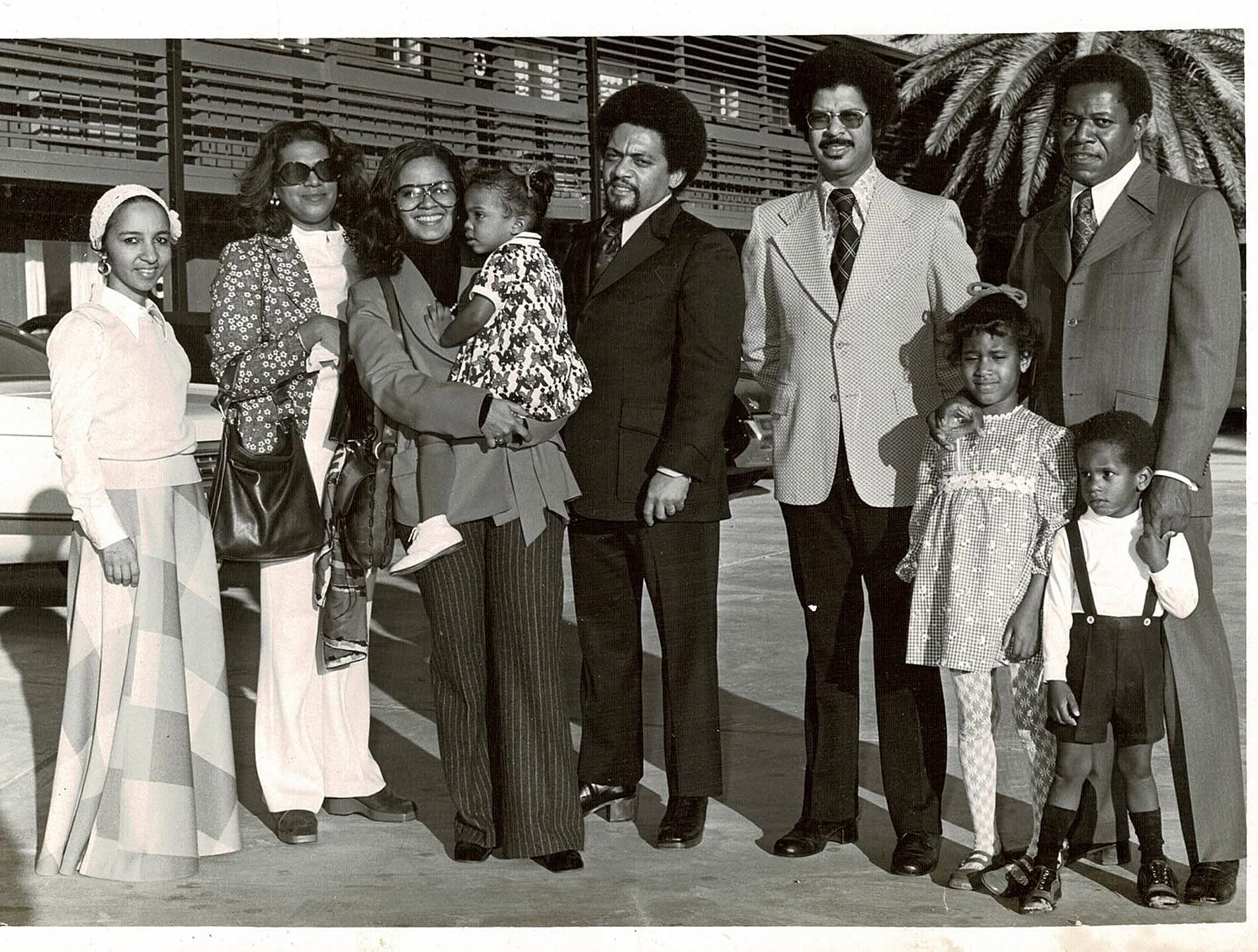 Black-and-white group portrait of eight adults and children in period suits and dresses outdoors.