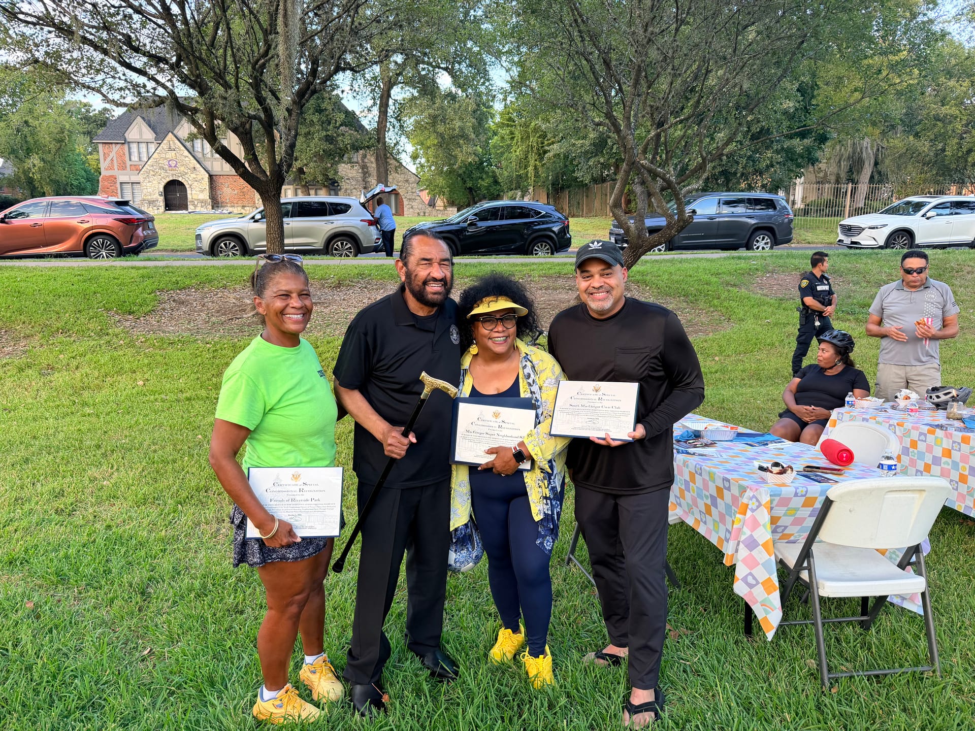 U.S. Representative Al Green, holding a cane, stands on the lawn at Riverside Park with RCA Vice President Sharon Evans-Brooks, in a neon green shirt, Tomoro Bell, in a yellow jacket, and South MacGregor Civic Club President Al Loyd, in a black cap. They hold Certificates of Special Congressional Recognition for Friends of Riverside Park, MacGregor Super Neighborhood 83 and South MacGregor Civic Club.