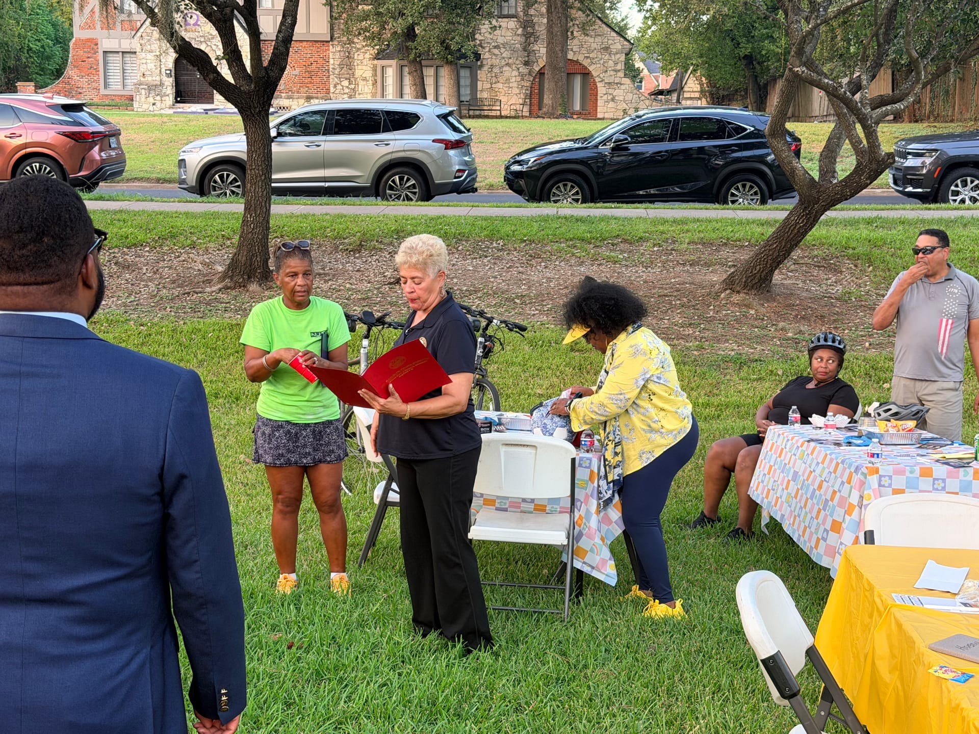 Council Member Carolyn Evans-Shabazz, District D, reads from a red folder beside RCA Vice President Sharon Evans-Brooks, in a neon green shirt, while Tomoro Bell, in a yellow jacket, sets out items at a nearby table.
