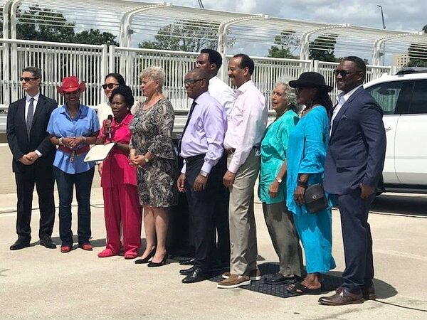 Row of officials and residents posing on a bridge while one person speaks into a microphone.