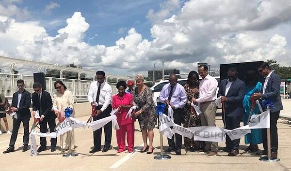 Group of officials cutting a ceremonial ribbon with scissors on a new pedestrian bridge.
