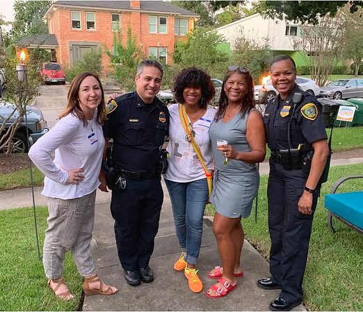 Three residents pose with two uniformed police officers on a sidewalk in front of a brick home.